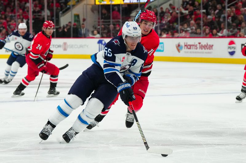 Mar 2, 2024; Raleigh, North Carolina, USA; Winnipeg Jets center Mark Scheifele (55) skates with the puck inside Carolina Hurricanes defenseman Brady Skjei (76) during the second period at PNC Arena. Mandatory Credit: James Guillory-USA TODAY Sports