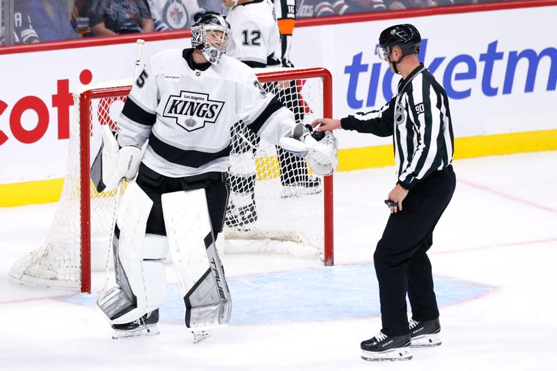 Oct 11, 2025; Winnipeg, Manitoba, CAN; Los Angeles Kings goaltender Darcy Kuemper (35) hands the puck to linesman Travis Tooney (90) during a game against the Winnipeg Jets in the third period  at Canada Life Centre. Mandatory Credit: James Carey Lauder-Imagn Images