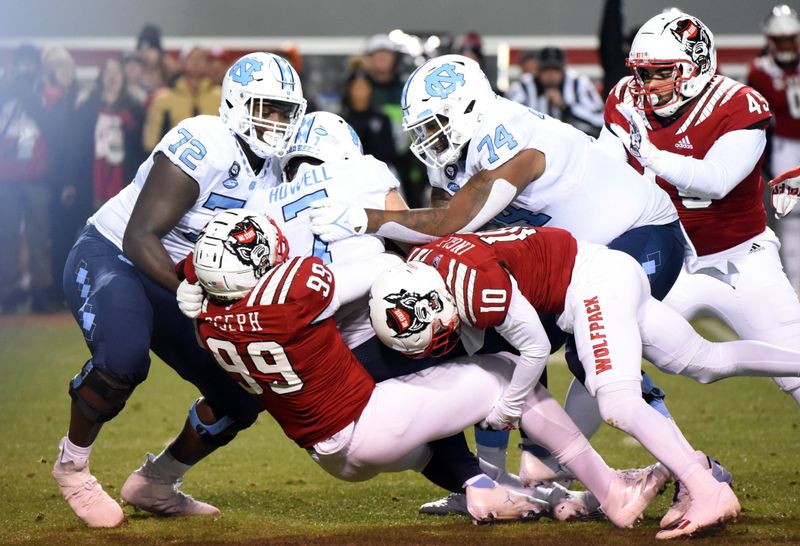 Nov 26, 2021; Raleigh, North Carolina, USA; North Carolina Tar Heels quarterback Sam Howell (7) is sacked by North Carolina State Wolfpack defensive end Joseph Boletepeli (99) and safety Tanner Ingle (10) during the first half at Carter-Finley Stadium. Mandatory Credit: Rob Kinnan-USA TODAY Sports