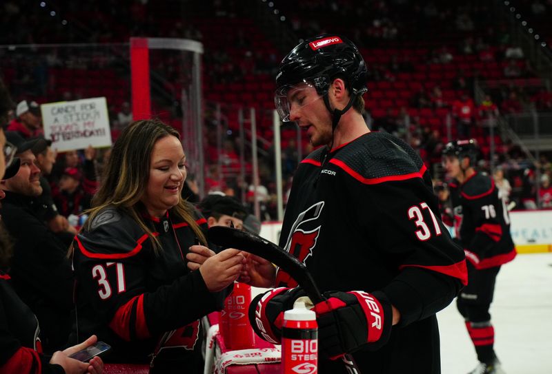 Jan 19, 2024; Raleigh, North Carolina, USA; Carolina Hurricanes right wing Andrei Svechnikov (37) signs an autograph for a fan on the bench before the game against the Detroit Red Wings at PNC Arena. Mandatory Credit: James Guillory-USA TODAY Sports