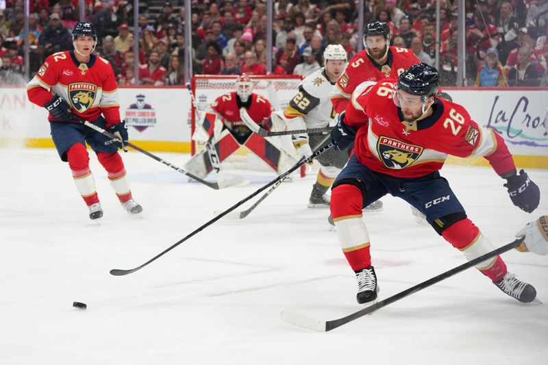 Oct 19, 2024; Sunrise, Florida, USA;  Florida Panthers defenseman Uvis Balinskis (26) tries to clear the puck against the Vegas Golden Knights during the first period at Amerant Bank Arena. Mandatory Credit: Jim Rassol-Imagn Images