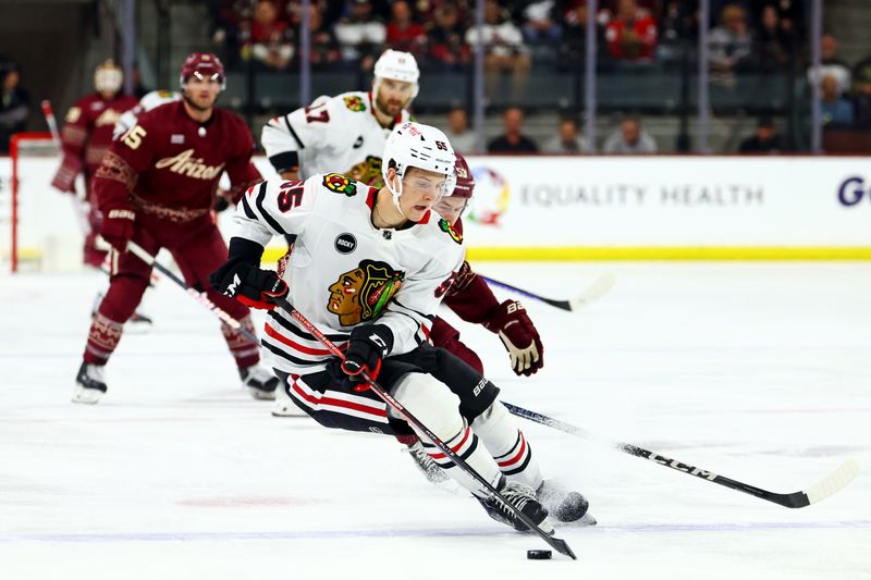 Mar 5, 2024; Tempe, Arizona, USA;  Chicago Blackhawks defenseman Kevin Korchinski (55) moves the puck against Arizona Coyotes left wing Michael Carcone (53) during the second period at Mullett Arena. Mandatory Credit: Mark J. Rebilas-USA TODAY Sports