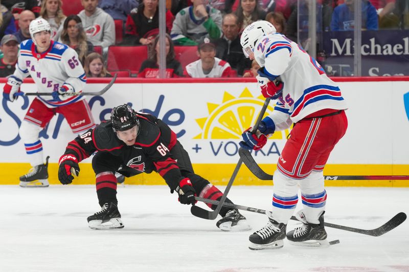 Nov 15, 2025; Raleigh, North Carolina, USA; Carolina Hurricanes defenseman Joel Nystrom (64) pokes the puck away from New York Rangers defenseman Adam Fox (23) during the first period at Lenovo Center. Mandatory Credit: James Guillory-Imagn Images