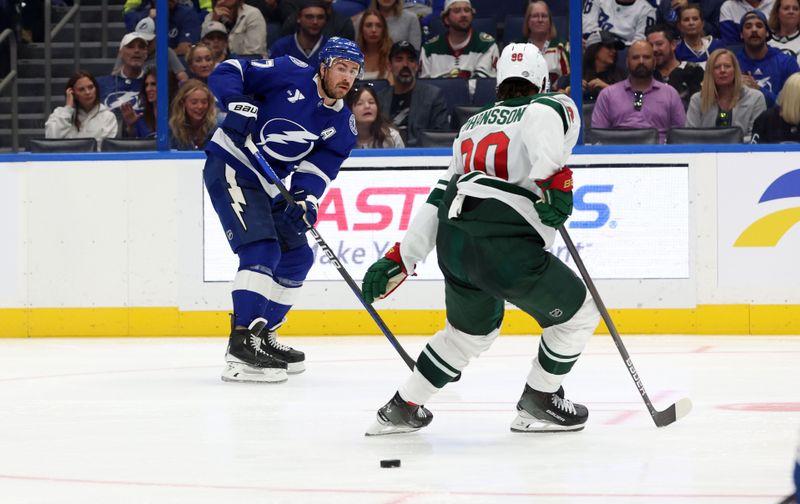 Oct 24, 2024; Tampa, Florida, USA; Tampa Bay Lightning defenseman Ryan McDonagh (27) passes the puck as Minnesota Wild center Marcus Johansson (90) defends during the third period at Amalie Arena. Mandatory Credit: Kim Klement Neitzel-Imagn Images