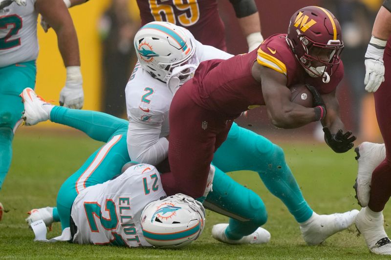 Washington Commanders running back Brian Robinson Jr. (8) is tackled by Miami Dolphins linebacker Bradley Chubb (2), top, and safety DeShon Elliott (21) during an NFL football game Sunday, Dec. 3, 2023, in Landover, Md. (AP Photo/Mark Schiefelbein)