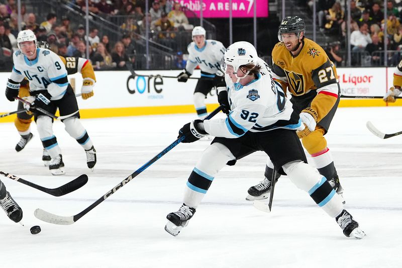 Nov 2, 2024; Las Vegas, Nevada, USA; Utah Hockey Club center Logan Cooley (92) controls the puck in front of Vegas Golden Knights defenseman Shea Theodore (27) during the first period at T-Mobile Arena. Mandatory Credit: Stephen R. Sylvanie-Imagn Images