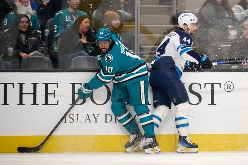 Dec 12, 2023; San Jose, California, USA; San Jose Sharks left wing Anthony Duclair (10) checks Winnipeg Jets defenseman Josh Morrissey (44) into the boards during the first period at SAP Center at San Jose. Mandatory Credit: Robert Edwards-USA TODAY Sports