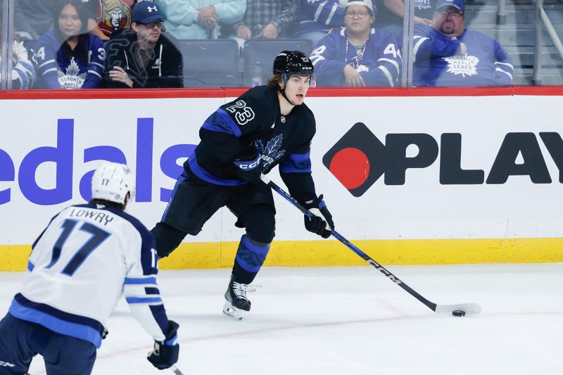 Oct 28, 2024; Winnipeg, Manitoba, CAN;  Toronto Maple Leafs forward Matthew Knies (23) controls the puck as Winnipeg Jets forward Adam Lowry (17) defends during the third period at Canada Life Centre. Mandatory Credit: Terrence Lee-Imagn Images