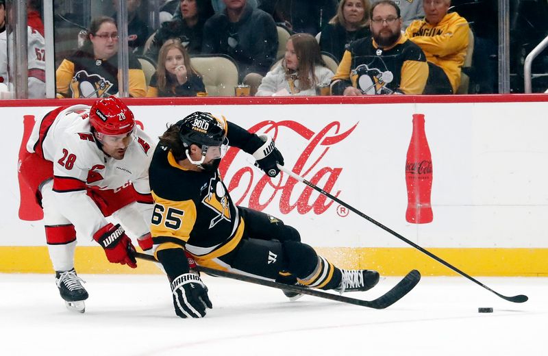 Oct 18, 2024; Pittsburgh, Pennsylvania, USA;  Carolina Hurricanes left wing William Carrier (28) commits a tripping penalty against Pittsburgh Penguins defenseman Erik Karlsson (65) during the second period at PPG Paints Arena. Mandatory Credit: Charles LeClaire-Imagn Images