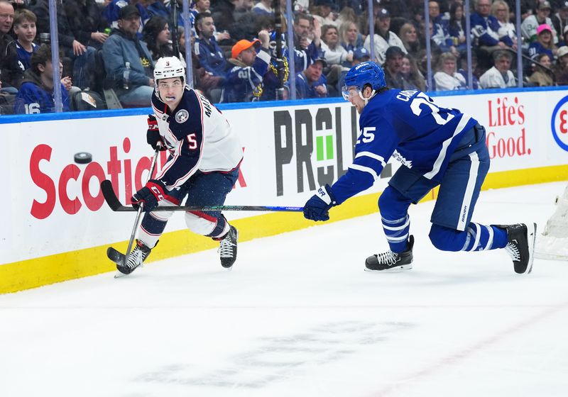 Apr 5, 2025; Toronto, Ontario, CAN; Toronto Maple Leafs defenseman Brandon Carlo (25) battles for the puck with Columbus Blue Jackets defenseman Denton Mateychuk (5) during the second period at Scotiabank Arena. Mandatory Credit: Nick Turchiaro-Imagn Images