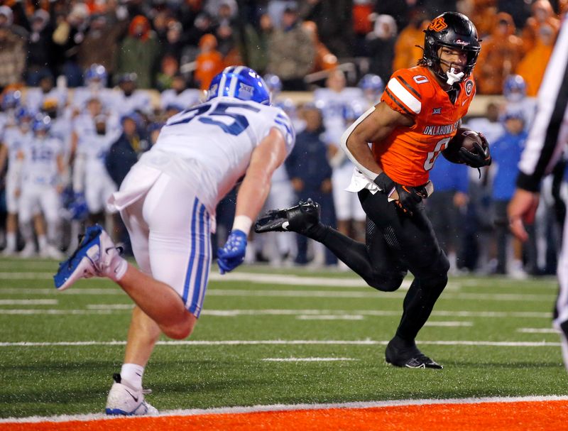 Nov 25, 2023; Stillwater, Oklahoma, USA;  Oklahoma State's Ollie Gordon II (0) scores a touchdown against BYU's Talan Alfrey (25) in the first overtime at Boone Pickens Stadium. Mandatory Credit: Sarah Phipps-USA TODAY Sports