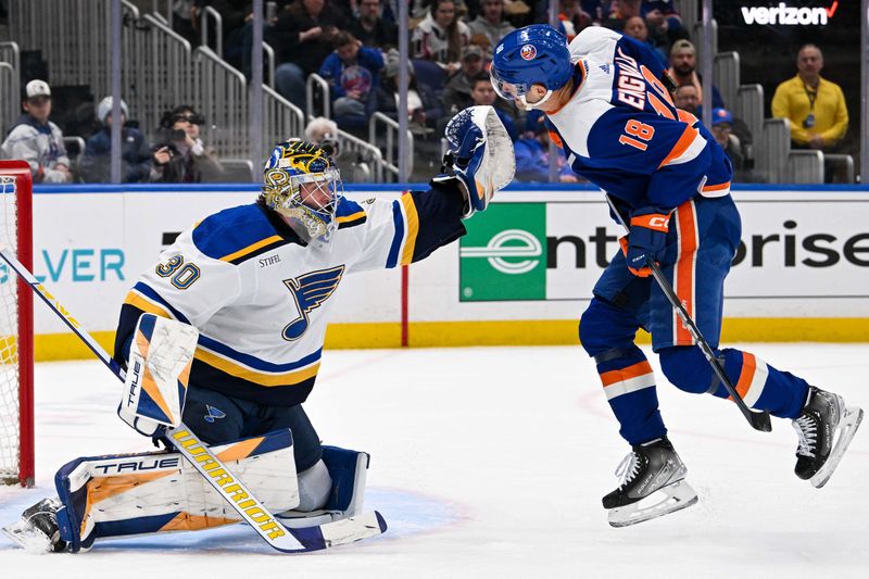 Mar 5, 2024; Elmont, New York, USA;  New York Islanders left wing Pierre Engvall (18) takes a puck to the back in front of St. Louis Blues goaltender Joel Hofer (30) during the second period at UBS Arena. Mandatory Credit: Dennis Schneidler-USA TODAY Sports