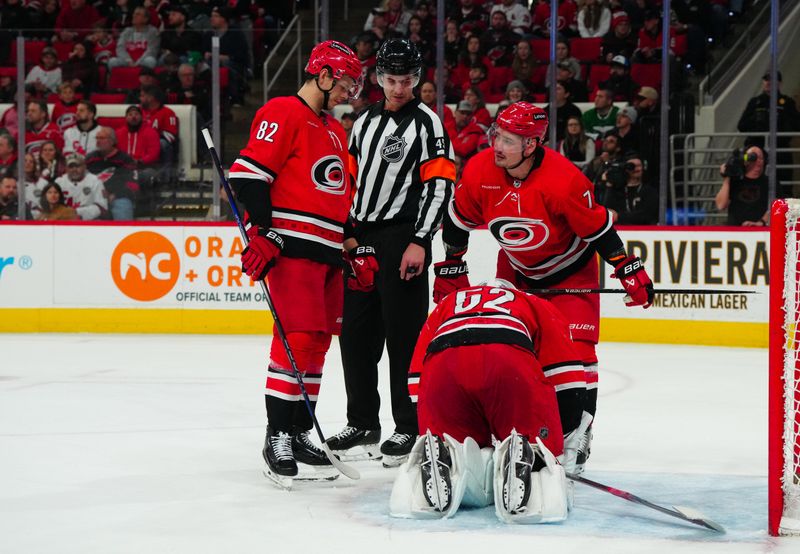 Jan 11, 2024; Raleigh, North Carolina, USA; Carolina Hurricanes goaltender Pyotr Kochetkov (52) kneels on the ice next to defenseman Dmitry Orlov (7) and center Jesperi Kotkaniemi (82) with referee Cody Beach (45) against the Anaheim Ducks during the second period at PNC Arena. Mandatory Credit: James Guillory-USA TODAY Sports