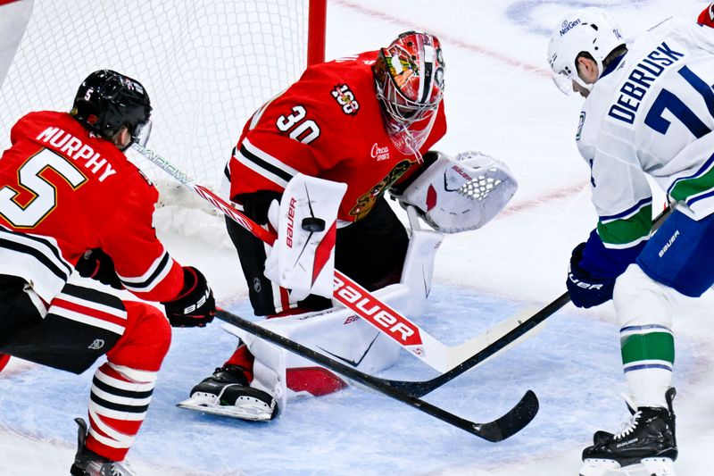 Oct 17, 2025; Chicago, Illinois, USA;  Vancouver Canucks left wing Jake Debrusk (74) scores past Chicago Blackhawks goaltender Spencer Knight (30) and  defenseman Connor Murphy (5) during the second period at the United Center. Mandatory Credit: Matt Marton-Imagn Images