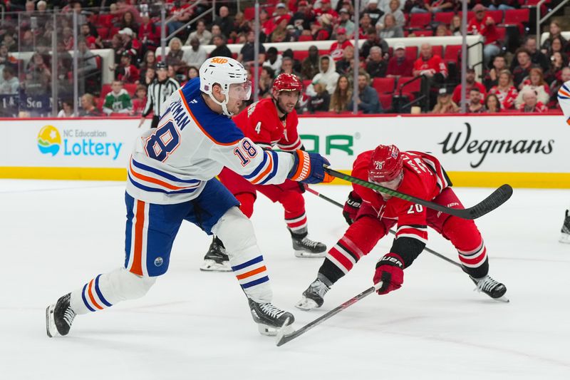 Nov 15, 2025; Raleigh, North Carolina, USA;  Edmonton Oilers left wing Zach Hyman (18) takes a shot past Carolina Hurricanes defenseman Sean Walker (26) during the second period at Lenovo Center. Mandatory Credit: James Guillory-Imagn Images