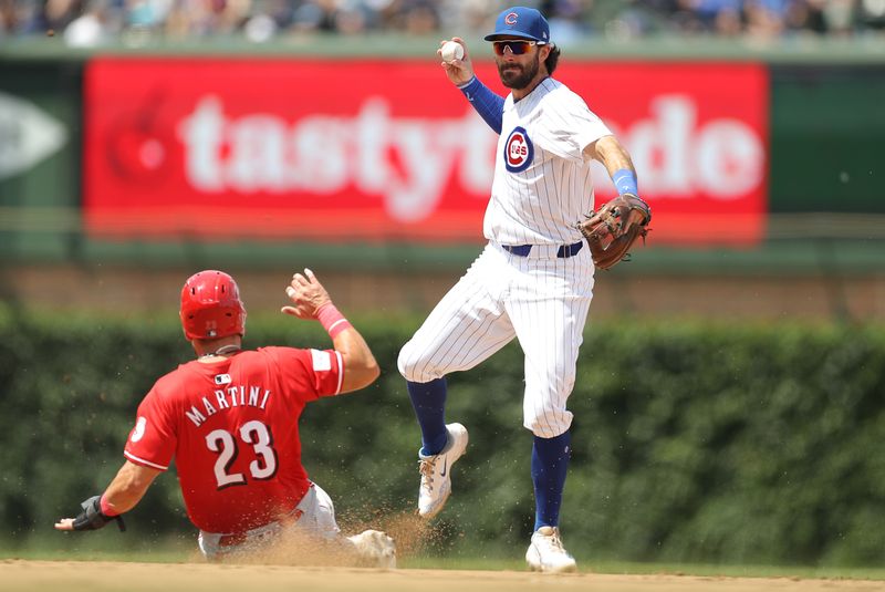 May 31, 2024; Chicago, Illinois, USA; Cincinnati Reds outfielder Nick Martini (23) slides as Chicago Cubs shortstop Dansby Swanson (7) throws the ball to first base for a double play during the fourth inning at Wrigley Field. Mandatory Credit: Melissa Tamez-USA TODAY Sports