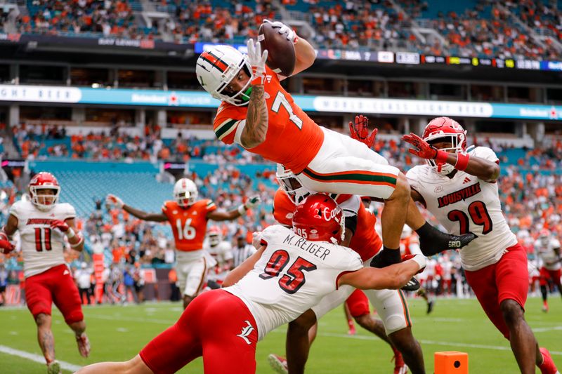 Nov 18, 2023; Miami Gardens, Florida, USA; Miami Hurricanes wide receiver Xavier Restrepo (7) leaps over Louisville Cardinals defensive lineman Mason Reiger (95) for a touchdown during the first quarter at Hard Rock Stadium. Mandatory Credit: Sam Navarro-USA TODAY Sports