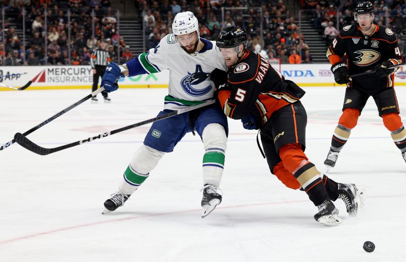 Mar 3, 2024; Anaheim, California, USA; Vancouver Canucks left wing Phillip Di Giuseppe (34) and Anaheim Ducks defenseman Urho Vaakanainen (5) fight for the puck during the third period at Honda Center. Mandatory Credit: Jason Parkhurst-USA TODAY Sports