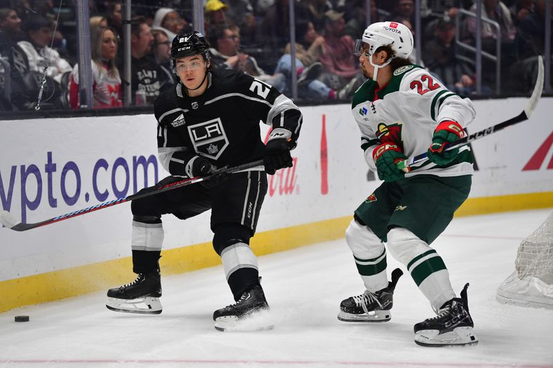 Mar 20, 2024; Los Angeles, California, USA; Los Angeles Kings defenseman Jordan Spence (21) moves the puck against Minnesota Wild center Marat Khusnutdinov (22) during the first period at Crypto.com Arena. Mandatory Credit: Gary A. Vasquez-USA TODAY Sports