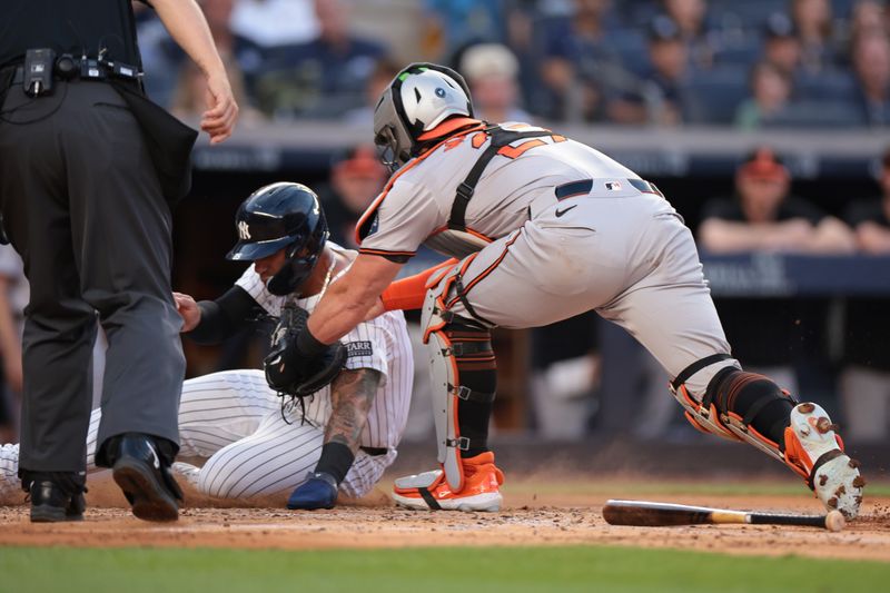 Jun 18, 2024; Bronx, New York, USA; Baltimore Orioles catcher James McCann (27) tags out New York Yankees second baseman Gleyber Torres (25) at home plate during the second inning at Yankee Stadium. Mandatory Credit: Vincent Carchietta-USA TODAY Sports