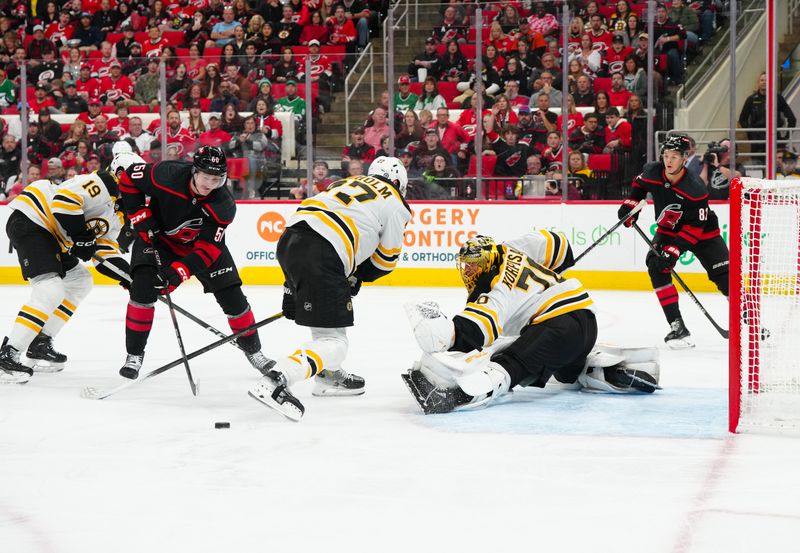 Oct 31, 2024; Raleigh, North Carolina, USA;  Boston Bruins goaltender Joonas Korpisalo (70) with defenseman Hampus Lindholm (27) watch the puck against Carolina Hurricanes left wing Eric Robinson (50) during the third period at Lenovo Center. Mandatory Credit: James Guillory-Imagn Images