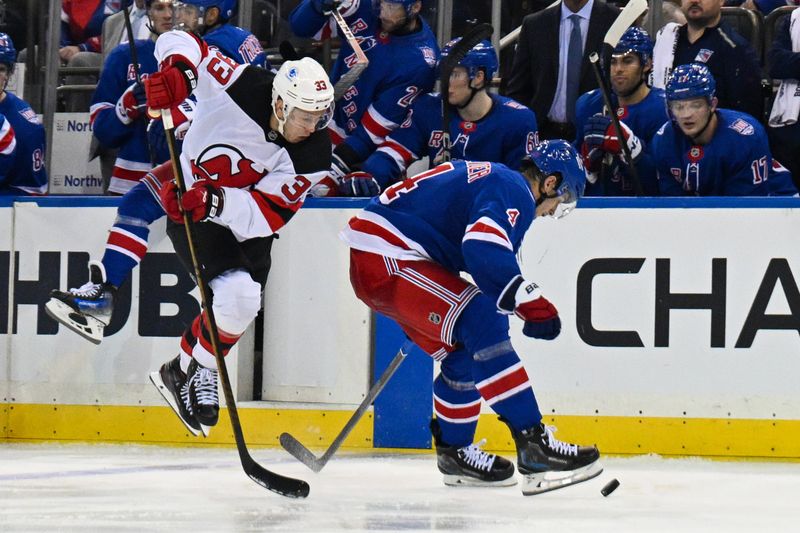 Oct 2, 2025; New York, New York, USA;  New Jersey Devils left wing Evgenii Dadonov (33) jumps over New York Rangers defenseman Braden Schneider (4) during the third period at Madison Square Garden. Mandatory Credit: Dennis Schneidler-Imagn Images