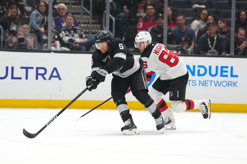 Nov 1, 2025; Los Angeles, California, USA; Los Angeles Kings defenseman Cody Ceci (5) and New Jersey Devils center Jack Hughes (86) reach for the puck in the first period at Crypto.com Arena. Mandatory Credit: Kirby Lee-Imagn Images
