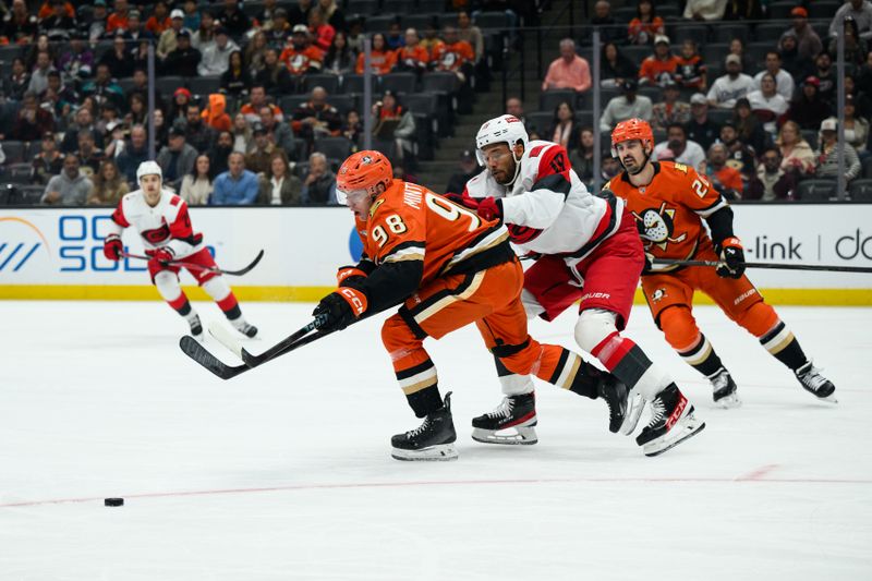 Oct 16, 2025; Anaheim, California, USA; Anaheim Ducks defenseman Pavel Mintyukov (98) tries to control the puck while under pressure from Carolina Hurricanes defenseman K'Andre Miller (19) during the first period at Honda Center. Mandatory Credit: William Liang-Imagn Images