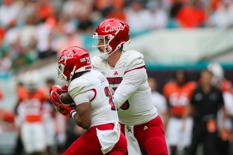 Nov 18, 2023; Miami Gardens, Florida, USA; Louisville Cardinals quarterback Jack Plummer (13) hands the football to running back Jawhar Jordan (25) against the Miami Hurricanes during the first quarter at Hard Rock Stadium. Mandatory Credit: Sam Navarro-USA TODAY Sports