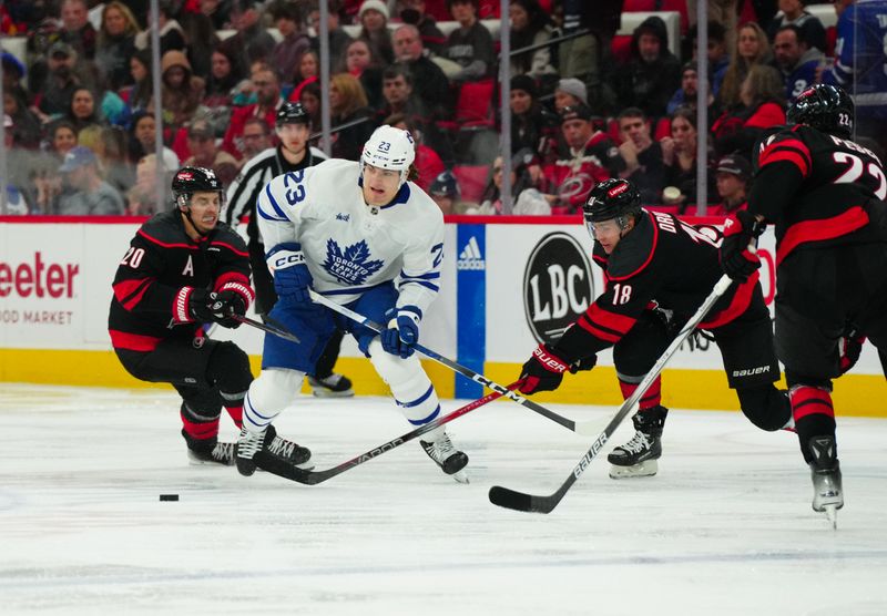 Mar 24, 2024; Raleigh, North Carolina, USA;  Toronto Maple Leafs left wing Matthew Knies (23) tries to skate with the puck past Carolina Hurricanes center Sebastian Aho (20) and center Jack Drury (18) during the second period at PNC Arena. Mandatory Credit: James Guillory-USA TODAY Sports