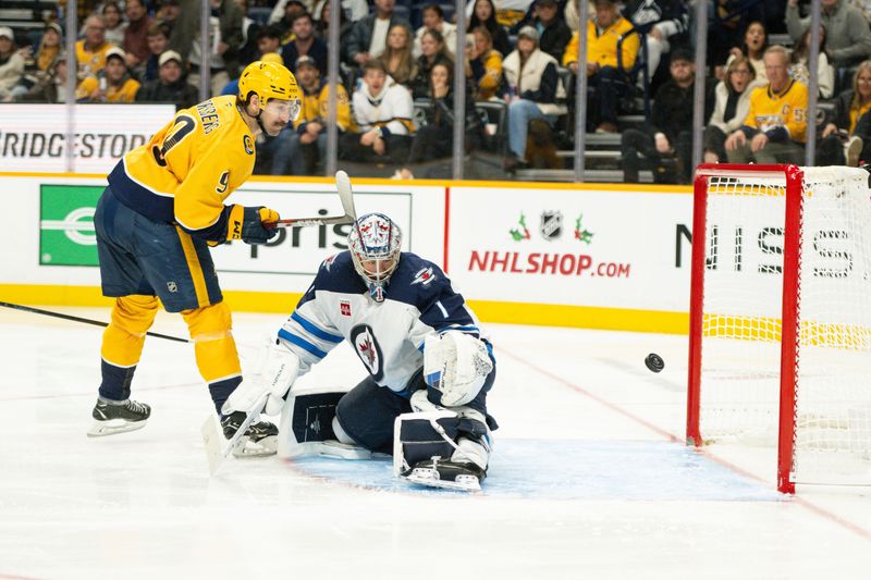 Nov 23, 2024; Nashville, Tennessee, USA;  Winnipeg Jets goaltender Eric Comrie (1) blocks the shoot if Nashville Predators left wing Filip Forsberg (9) during the third period at Bridgestone Arena. Mandatory Credit: Steve Roberts-Imagn Images