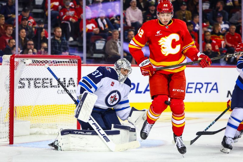 Oct 4, 2024; Calgary, Alberta, CAN; Calgary Flames left wing Samuel Honzek (42) blocks a shot in front of Winnipeg Jets goaltender Connor Hellebuyck (37) during the second period at Scotiabank Saddledome. Mandatory Credit: Sergei Belski-Imagn Images