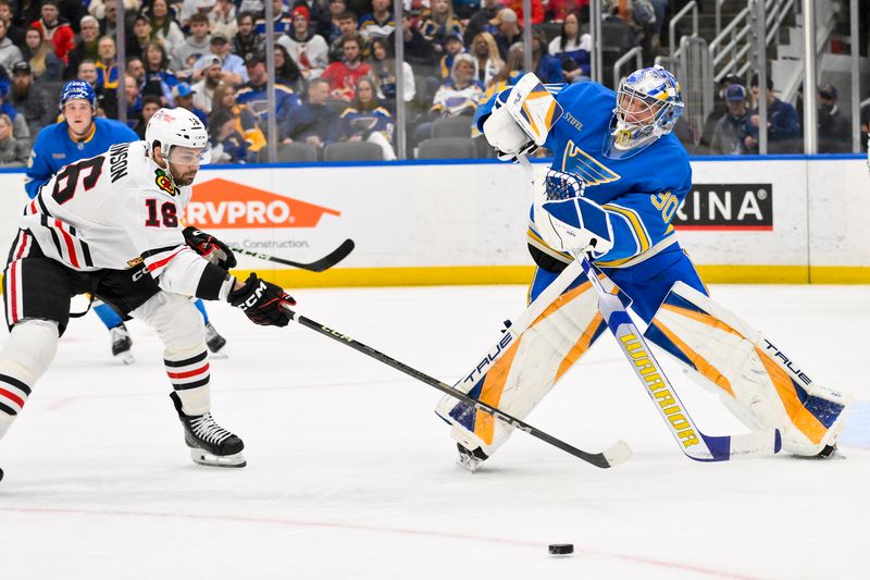 Mar 22, 2025; St. Louis, Missouri, USA;  St. Louis Blues goaltender Joel Hofer (30) clears the puck past Chicago Blackhawks center Jason Dickinson (16) during the first period at Enterprise Center. Mandatory Credit: Jeff Curry-Imagn Images