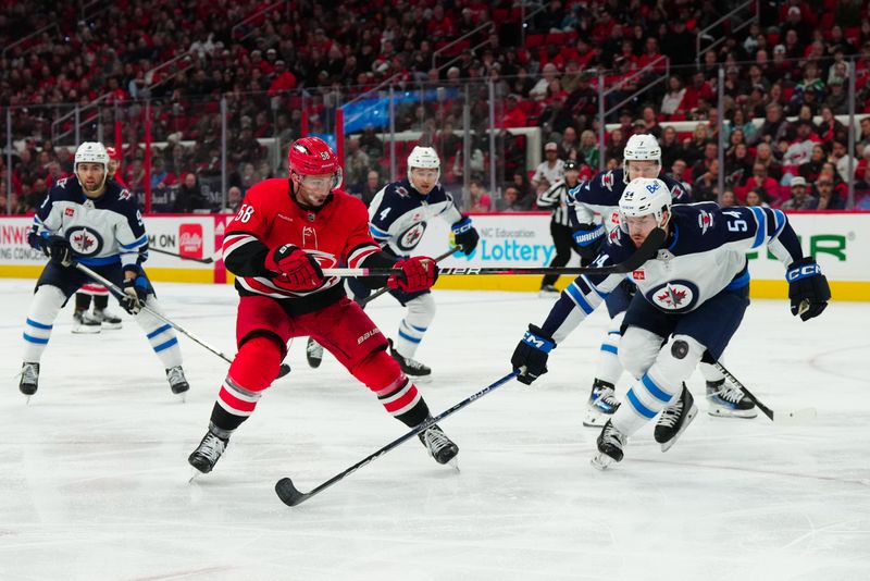 Mar 2, 2024; Raleigh, North Carolina, USA; Carolina Hurricanes left wing Michael Bunting (58) gets the shot away against Winnipeg Jets defenseman Dylan Samberg (54) during the third period at PNC Arena. Mandatory Credit: James Guillory-USA TODAY Sports