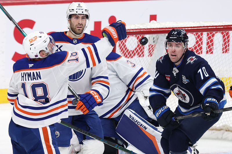Dec 29, 2025; Winnipeg, Manitoba, CAN; Edmonton Oilers left wing Zach Hyman (18) and Winnipeg Jets left wing Tanner Pearson (70) eye a flying puck in the third period at Canada Life Centre. Mandatory Credit: James Carey Lauder-Imagn Images
