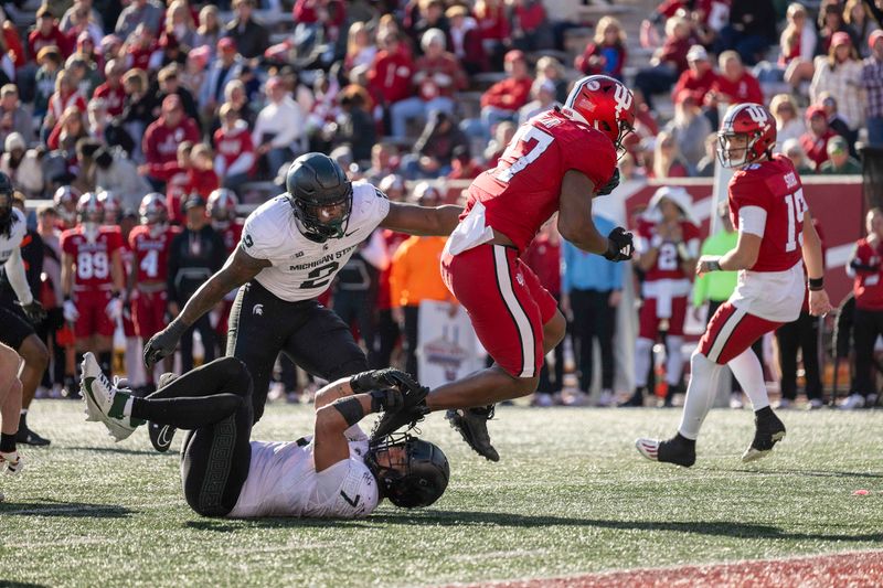 Nov 18, 2023; Bloomington, Indiana, USA; Indiana Hoosiers running back Trent Howland (27) jumps over Michigan State Spartans linebacker Aaron Brule (7) and past defensive lineman Khris Bogle (2) during the second half at Memorial Stadium. Mandatory Credit: Marc Lebryk-USA TODAY Sports