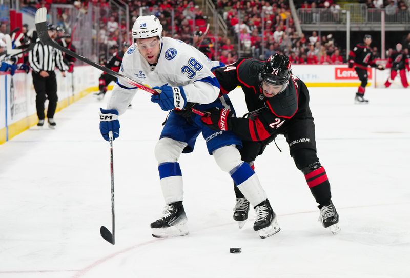 Oct 11, 2024; Raleigh, North Carolina, USA;  Carolina Hurricanes center Seth Jarvis (24) and Tampa Bay Lightning left wing Brandon Hagel (38) battle over the puck during the first period at PNC Arena. Mandatory Credit: James Guillory-Imagn Images