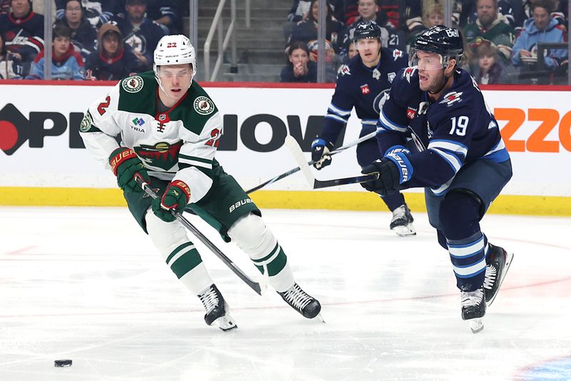Dec 27, 2025; Winnipeg, Manitoba, CAN; Winnipeg Jets center Jonathan Toews (19) clears the puck past Minnesota Wild right wing Danila Yurov (22) in the first period at Canada Life Centre. Mandatory Credit: James Carey Lauder-Imagn Images
