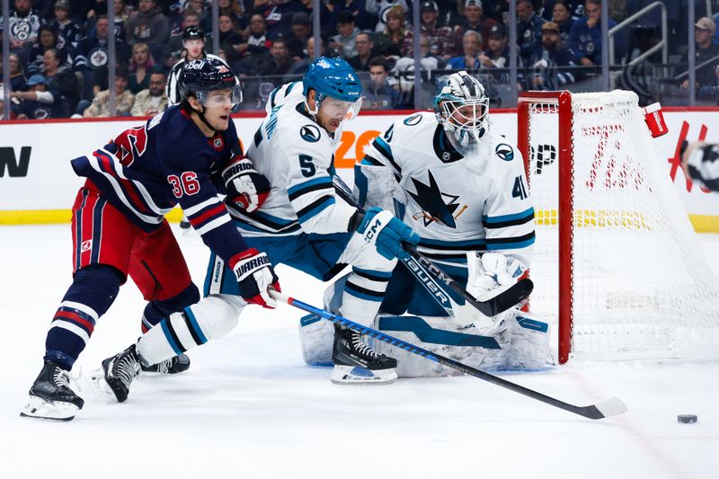 Oct 18, 2024; Winnipeg, Manitoba, CAN;  Winnipeg Jets forward Morgan Barron (36) and San Jose Sharks defenseman Matt Benning (5) chase the puck in front of San Jose Sharks goalie Vitek Vanecek (41) during the second period at Canada Life Centre. Mandatory Credit: Terrence Lee-Imagn Images