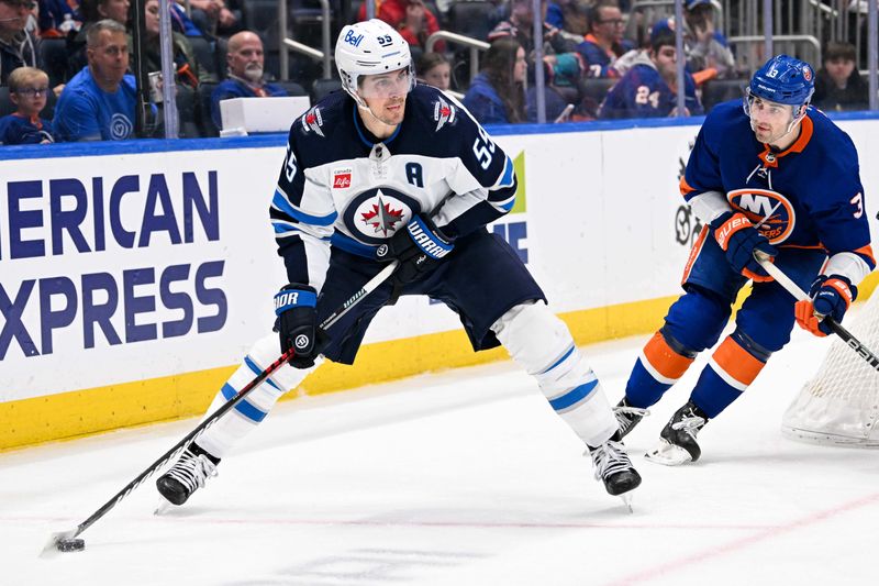 Mar 23, 2024; Elmont, New York, USA;  Winnipeg Jets center Mark Scheifele (55) skates with the puck chased by New York Islanders defenseman Adam Pelech (3) during the third period at UBS Arena. Mandatory Credit: Dennis Schneidler-USA TODAY Sports