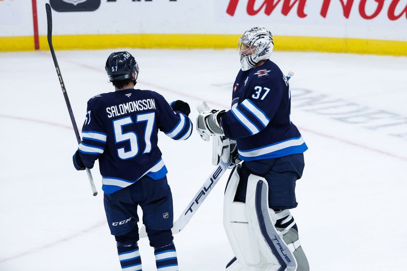 Oct 2, 2024; Winnipeg, Manitoba, CAN;  Winnipeg Jets goalie Connor Hellebuyck (37) is congratulated by Winnipeg Jets defenseman Elias Salomonsson (57) on his win against the Calgary Flames at the end of the third period at Canada Life Centre. Mandatory Credit: Terrence Lee-Imagn Images