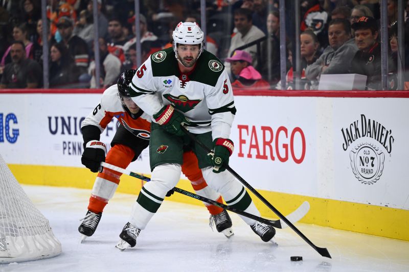 Oct 26, 2024; Philadelphia, Pennsylvania, USA; Minnesota Wild defenseman Jake Middleton (5) controls the puck against Philadelphia Flyers defenseman Travis Sanheim (6) in the third period at Wells Fargo Center. Mandatory Credit: Kyle Ross-Imagn Images