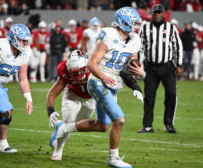 Nov 25, 2023; Raleigh, North Carolina, USA; North Carolina Tar Heels quarterback Drake Maye (10) runs the ball against North Carolina State Wolfpack defensive end Davin Vann (1) during the first half at Carter-Finley Stadium. Mandatory Credit: Rob Kinnan-USA TODAY Sports