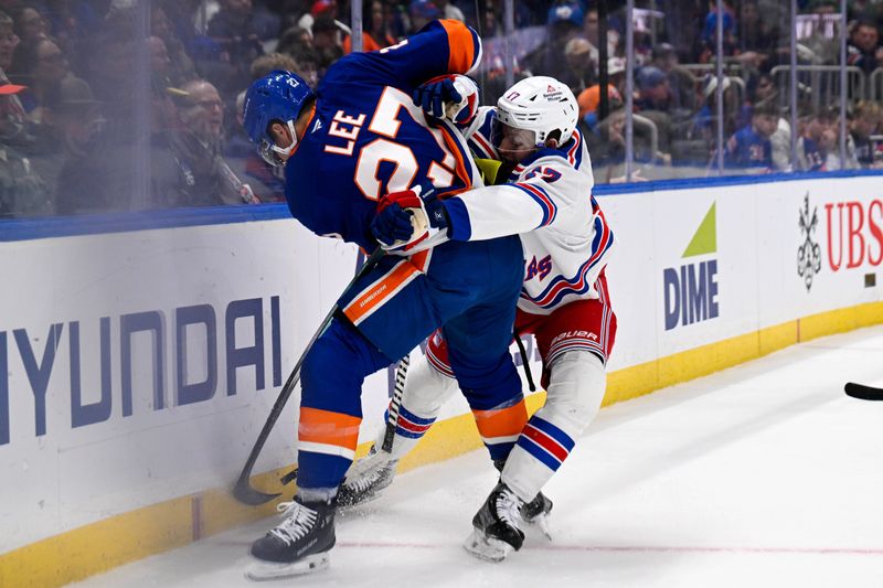 Feb 25, 2025; Elmont, New York, USA;  New York Islanders left wing Anders Lee (27) and New York Rangers defenseman Will Borgen (17) battle for the puck along the boards during the second period at UBS Arena. Mandatory Credit: Dennis Schneidler-Imagn Images