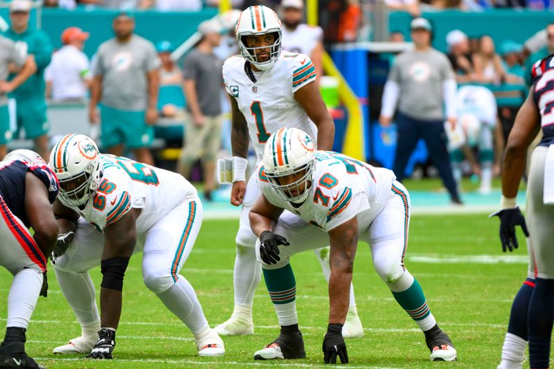 Miami Dolphins quarterback Tua Tagovailoa (1) prepares to take the snap of the ball at the line of scrimmage with Miami Dolphins offensive lineman Robert Jones (65) and Miami Dolphins tackle Kendall Lamm (70) during an NFL football game against the New England Patriots, Sunday, Oct. 29, 2023, in Miami Gardens, Fla. (AP Photo/Doug Murray)