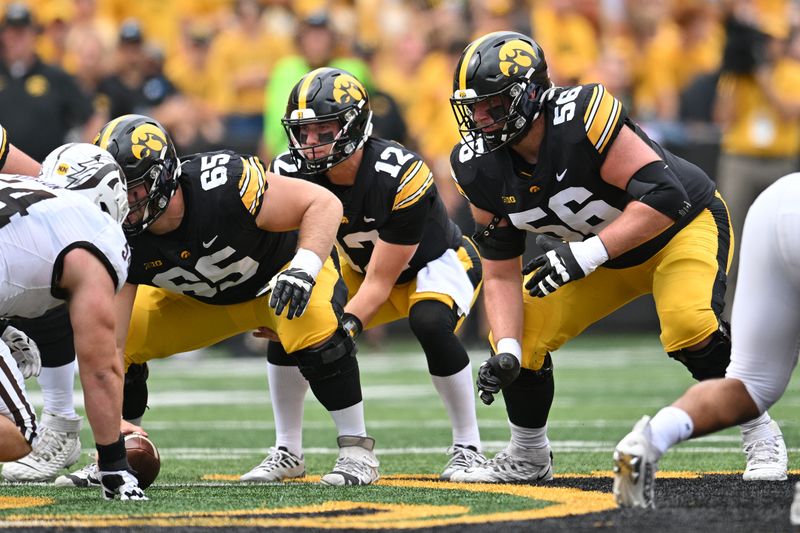 Sep 16, 2023; Iowa City, Iowa, USA; Iowa Hawkeyes quarterback Cade McNamara (12), offensive lineman Logan Jones (65) and offensive lineman Nick DeJong (56) prepare for the snap against the Western Michigan Broncos during the first quarter at Kinnick Stadium. Mandatory Credit: Jeffrey Becker-USA TODAY Sports