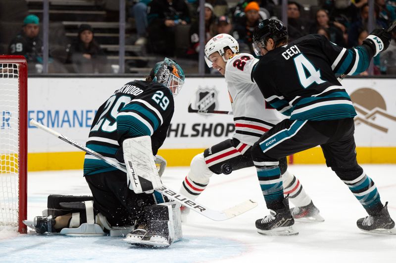 Oct 31, 2024; San Jose, California, USA; San Jose Sharks goaltender Mackenzie Blackwood (29) blocks the puck as Chicago Blackhawks center Philipp Kurashev (23) and defenseman Cody Ceci (4) vie for position during the first period at SAP Center at San Jose. Mandatory Credit: D. Ross Cameron-Imagn Images