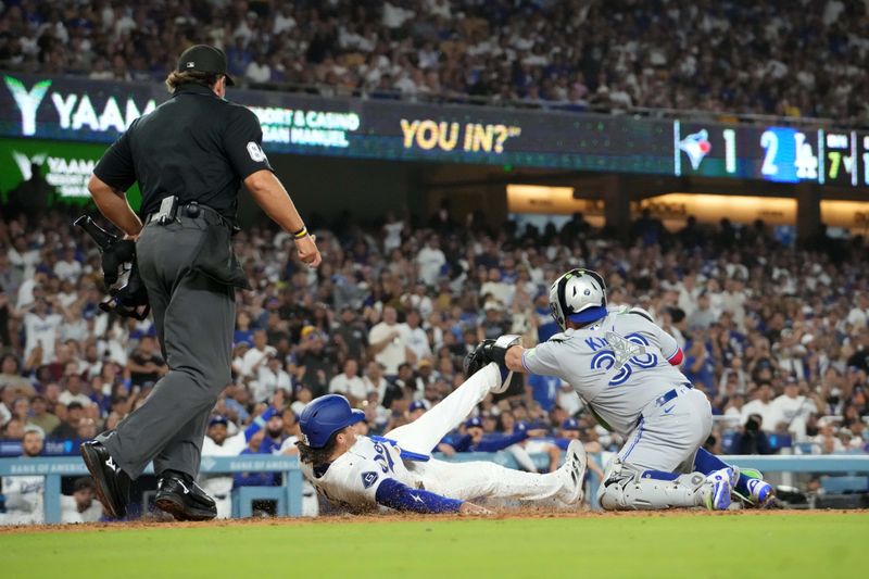 Aug 8, 2025; Los Angeles, California, USA; Los Angeles Dodgers second baseman Alex Freeland (76) slides into home plate to beat a throw to Toronto Blue Jays catcher Alejandro Kirk (30) to score in the seventh inning as home plate umpire John Libka (84) watches at Dodger Stadium. Mandatory Credit: Kirby Lee-Imagn Images