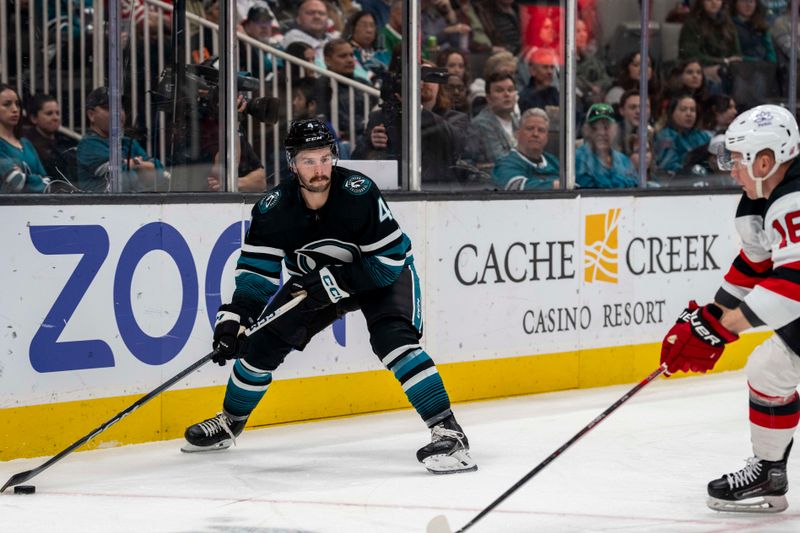 Feb 27, 2024; San Jose, California, USA;  San Jose Sharks defenseman Kyle Burroughs (4) controls the puck behind the net against New Jersey Devils left wing Ondrej Palat (18) \d1p] at SAP Center at San Jose. Mandatory Credit: Neville E. Guard-USA TODAY Sports