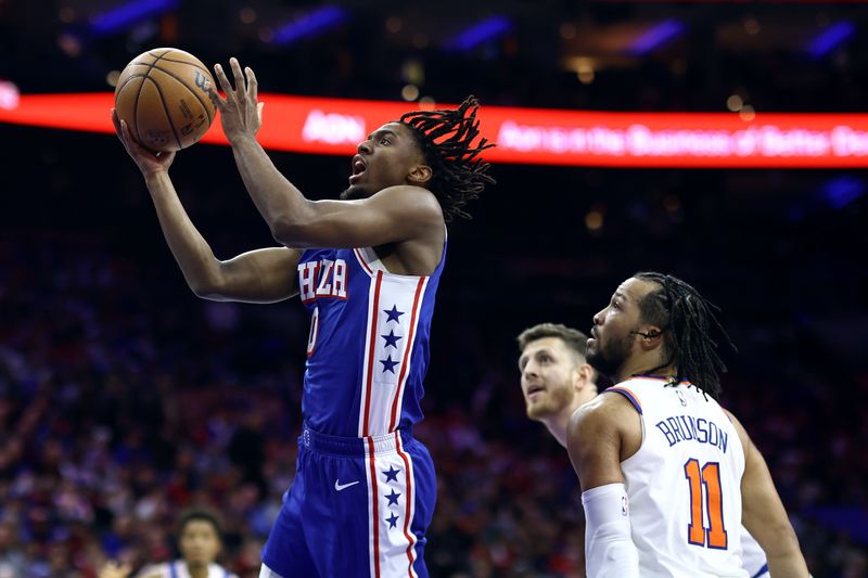 PHILADELPHIA, PENNSYLVANIA - APRIL 25: Tyrese Maxey #0 of the Philadelphia 76ers shoots a lay up past Isaiah Hartenstein #55 and Jalen Brunson #11 of the New York Knicks during the third quarter of game three of the Eastern Conference First Round Playoffs at the Wells Fargo Center on April 25, 2024 in Philadelphia, Pennsylvania. NOTE TO USER: User expressly acknowledges and agrees that, by downloading and/or using this Photograph, user is consenting to the terms and conditions of the Getty Images License Agreement. (Photo by Tim Nwachukwu/Getty Images)